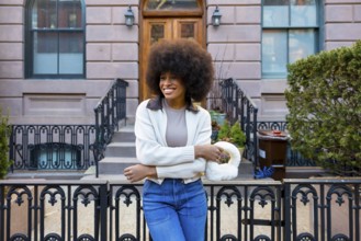 Smiling young woman with a large afro hairstyle and fashionable attire standing in front of a