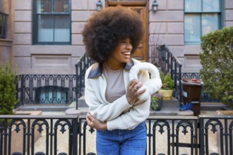 Happy black woman with afro hair laughing, holding furry earmuffs, and wearing jeans with a sweater