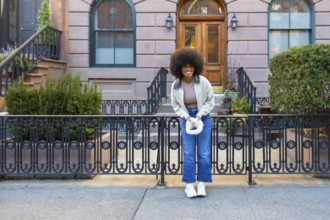 Smiling young black woman with afro hairstyle standing happily on a sidewalk in front of a classic