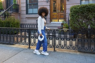 Happy young black woman walking on a sidewalk, smiling, and holding a plush handbag, showcasing