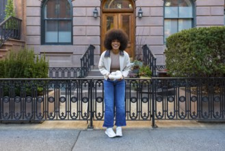 Cheerful smiling woman standing on a new york city street, holding white yarn in her hands,