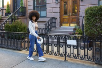 Happy young woman with an afro hairstyle walking on a sidewalk in front of brownstone buildings in