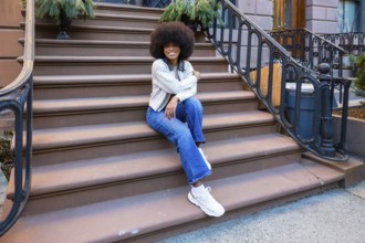 Young african american woman with afro hair sitting on a brownstone stoop in a new york city