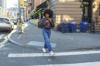 Young woman with afro hair and casual fashion attire confidently walking across a zebra crossing in