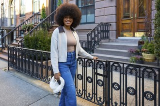 Young black woman with a large afro in jeans and a sweater, smiling confidently while standing on a