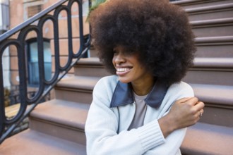African american woman with a beautiful afro hairstyle sitting and smiling on brownstone steps in