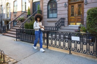 Young african american woman with afro hair smiling while walking along a new york city sidewalk