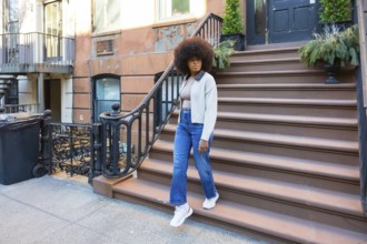 Young black woman with a stylish afro hairstyle walking down the steps of a traditional brownstone
