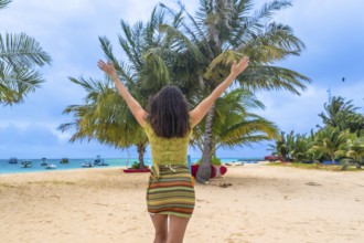 Woman standing on a white sand beach, raising arms to the sky, embracing joy and freedom during a