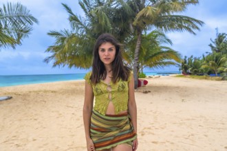 Young woman posing on a stunning tropical beach, standing in front of palm trees and turquoise