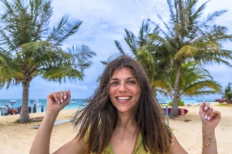 Young woman smiling with joy, celebrating her tropical beach vacation with swaying palm trees and