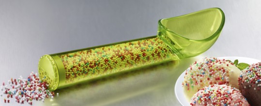 Yellow, transparent ice cream scoop filled with coloured sugar sprinkles, next to a plate with