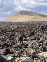 Hiking trail through lava rock to Caldera Blanca volcano against blue sky with white clouds, Mancha