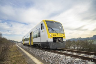 A train moves through open countryside on rails under a blue and white sky, taking off the Hermann