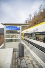 A train station in Calw in the Black Forest with a train and wooded landscape in the background,