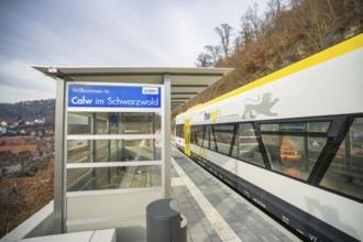 A modern train station in Calw with an outbound train surrounded by wooded hills, taking the