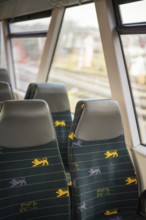 Two train seats with blue fabric and yellow lion patterns next to train windows in the interior,