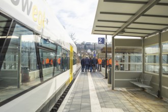 People standing in a group on a platform next to a train at a bus stop, the Hermann Hessebahn ride,