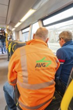 Back view of men on a train, one wearing an AVG work jacket, taking off the Hermann Hessebahn,