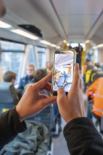 Man taking a photo with a smartphone in a busy train interior, taking the Hermann Hessebahn, Calw,