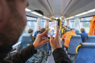 Person photographs the interior of a train and other passengers with a smartphone, Hermann
