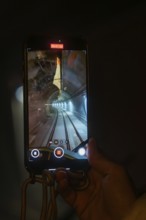 A smartphone shows the inside view of a tunnel crossed by a train, held by one hand, the Hermann