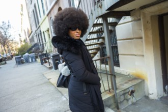 Young woman with big afro hairstyle wearing sunglasses and a fashionable black winter coat with fur