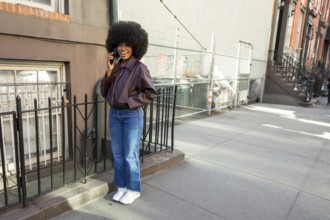 Young black woman with an afro hairstyle standing on a manhattan street, wearing a bomber jacket