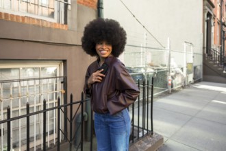 Young african american woman with a large afro hairstyle smiling, wearing a leather jacket and