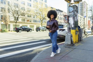 Young black woman smiling confidently, walking briskly on a manhattan city street, wearing a
