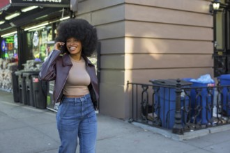 Young black woman with afro hairstyle walking manhattan sidewalk, smiling and chatting on