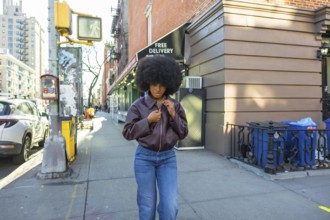 Young black woman with an afro hairstyle adjusting her brown leather jacket while standing on a