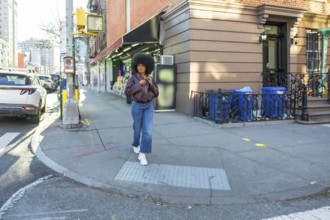 Young woman with natural afro hair walking confidently along a residential brownstone building on a
