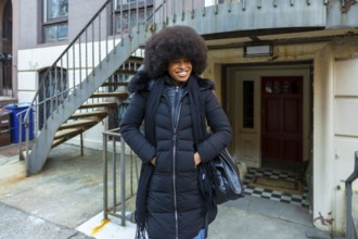 African american woman smiling while standing in front of a manhattan brownstone building. Wearing