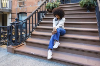 Young african american woman with an afro hairstyle sitting casually on brownstone stoop steps.