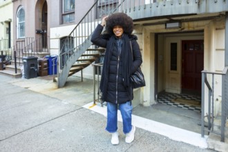 Joyful black woman with afro smiling confidently on a manhattan brownstone street in casual winter