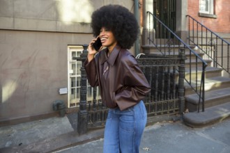 African american woman with an afro hairstyle smiling and communicating on a smartphone while