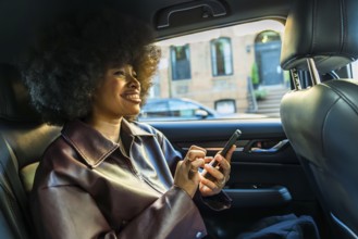 Young woman with afro hairstyle smiling, riding in the backseat of a car through new york city,