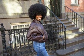Young african american woman smiling while posing with an afro hairstyle and brown bomber jacket