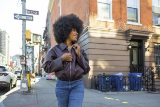 Young black woman with an afro hairstyle smiling while walking along a vibrant w 22nd street