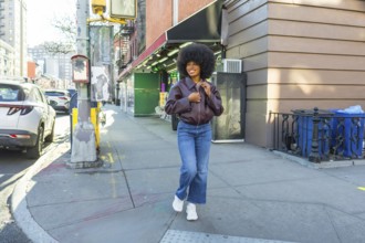 Young black woman with a vibrant afro smiling as she walks a sunny manhattan street in casual