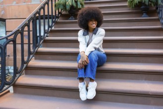 Young black woman sitting on brownstone steps in harlem, smiling and relaxed in casual street