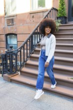 Smiling woman with afro hair descending brownstone steps in new york city, expressing joy and