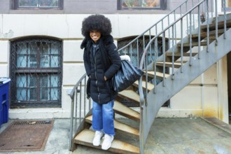 Happy black woman with an afro hairstyle smiling, standing on rusty metal stairs wearing a black