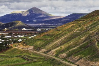 Hilly landscape with green slopes, mountains and a village under overcast skies, Yaiza Lanzarote