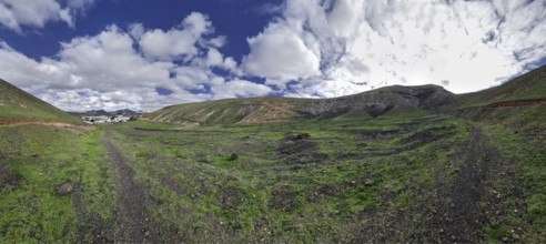 Wide landscape with trails and grassy hills under cloudy sky, Yaiza Lanzarote