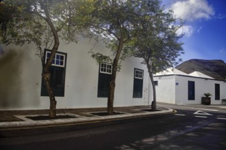 White building with green shutters and trees along the road, Yaiza Lanzarote