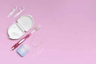 Top view of dental clear aligners, toothbrush, toothpicks and floss on pink background with copy
