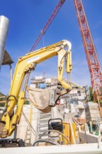 Large yellow excavator on a construction site surrounded by construction cranes, carpentry, new