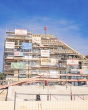 Large building under construction with scaffolding and various advertising banners as well as